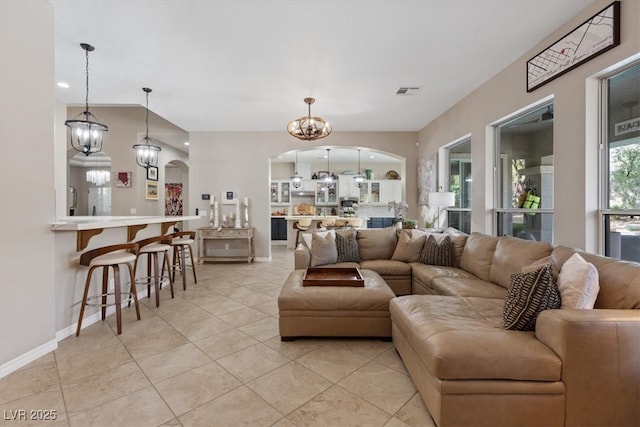 living area with arched walkways, light tile patterned floors, a notable chandelier, visible vents, and baseboards