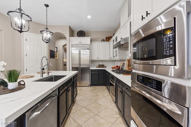 kitchen featuring stainless steel appliances, under cabinet range hood, white cabinetry, pendant lighting, and a sink