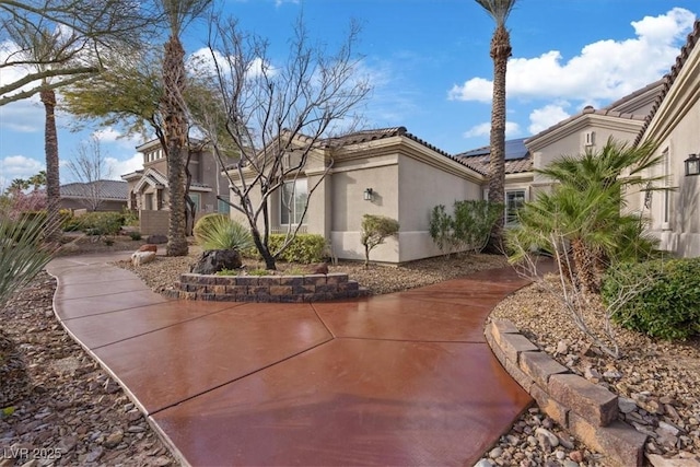 view of side of property with roof mounted solar panels, a tile roof, and stucco siding