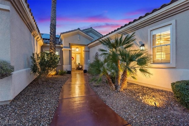 exterior entry at dusk with a tile roof and stucco siding