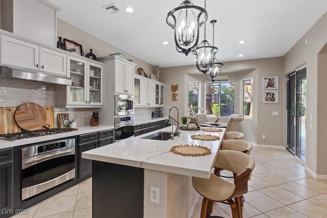 kitchen with a notable chandelier, under cabinet range hood, a breakfast bar, a sink, and appliances with stainless steel finishes