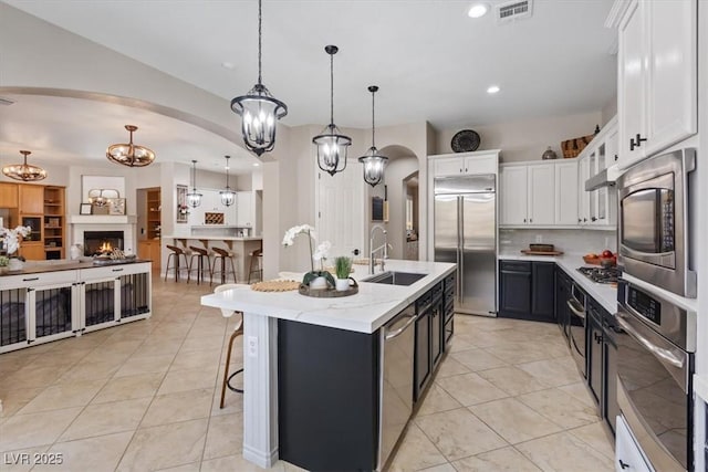 kitchen featuring arched walkways, visible vents, white cabinets, a sink, and built in appliances