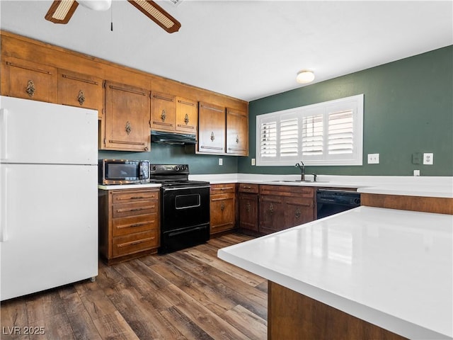 kitchen featuring under cabinet range hood, dark wood finished floors, light countertops, black appliances, and a sink