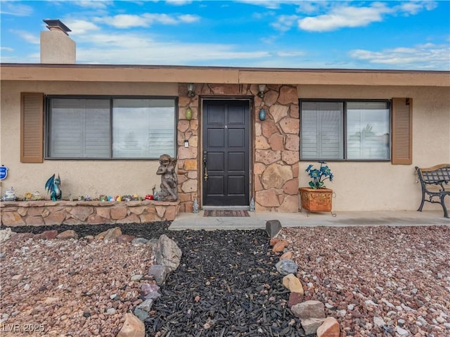 view of exterior entry featuring stucco siding and a chimney