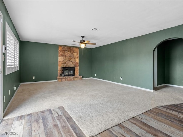 unfurnished living room with visible vents, a ceiling fan, arched walkways, a fireplace, and baseboards