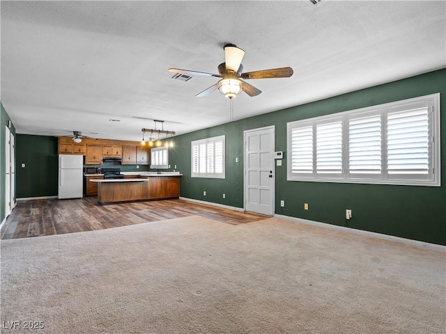 kitchen featuring visible vents, brown cabinets, open floor plan, dark carpet, and freestanding refrigerator