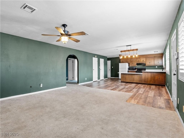 unfurnished living room featuring a ceiling fan, baseboards, visible vents, arched walkways, and light carpet