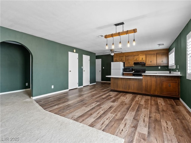 kitchen featuring range hood, brown cabinetry, a peninsula, black appliances, and open floor plan