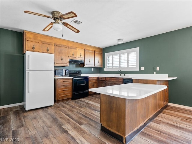 kitchen featuring visible vents, black appliances, a sink, under cabinet range hood, and a peninsula