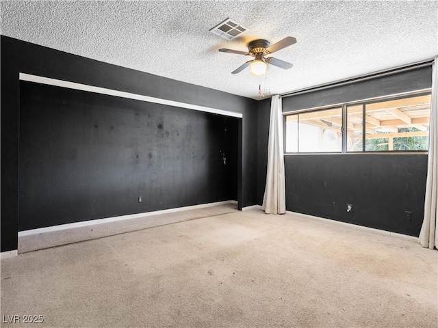 spare room featuring carpet, baseboards, visible vents, ceiling fan, and a textured ceiling