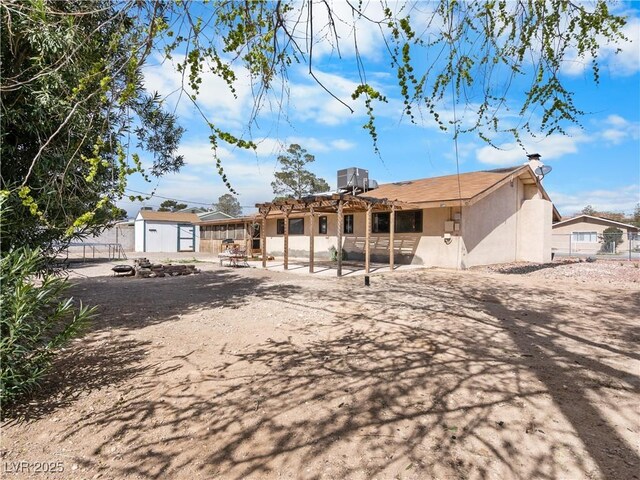 back of property with fence, stucco siding, an outdoor structure, a storage unit, and a patio