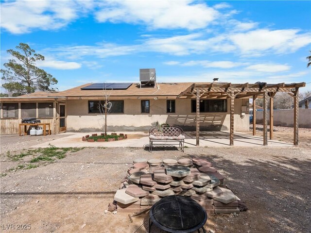 back of property with solar panels, an outdoor fire pit, central AC, a sunroom, and a patio