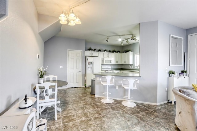 kitchen with white appliances, a breakfast bar, a peninsula, white cabinetry, and a notable chandelier