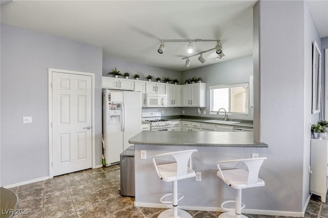 kitchen with white appliances, a breakfast bar, a sink, white cabinets, and dark countertops