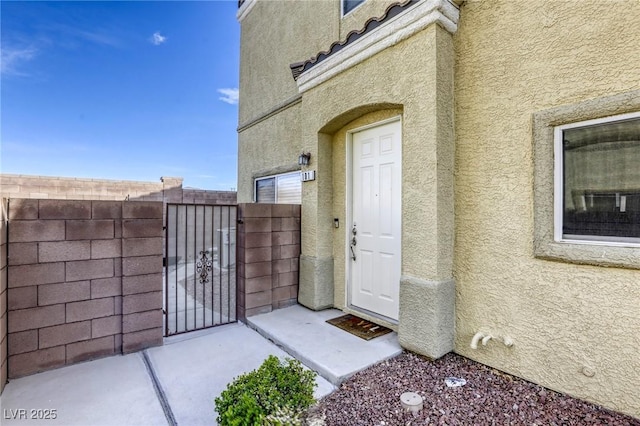 property entrance featuring a gate, fence, and stucco siding