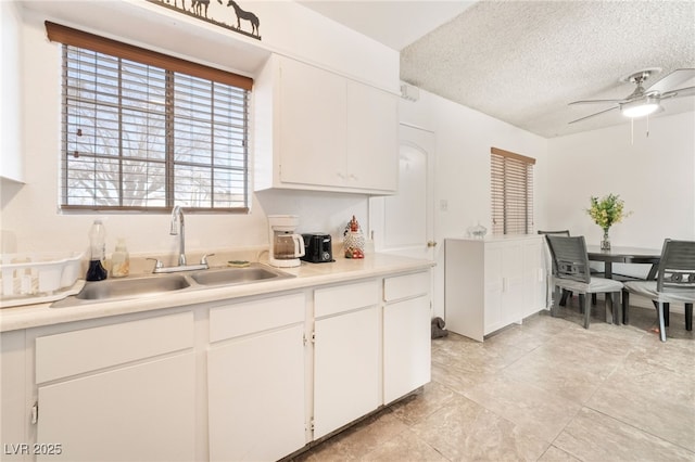 kitchen featuring a textured ceiling, light countertops, a sink, and white cabinetry