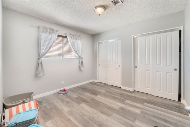 unfurnished bedroom with multiple closets, visible vents, a textured ceiling, wood finished floors, and baseboards