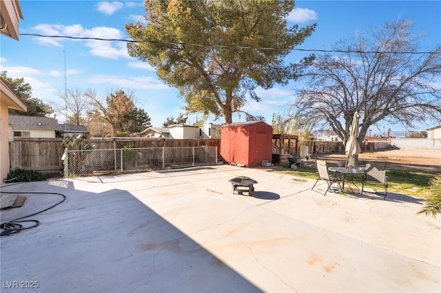 view of patio / terrace with a fire pit, a fenced backyard, a storage unit, and an outbuilding