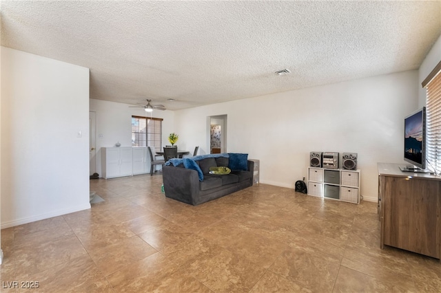 living room featuring baseboards, ceiling fan, visible vents, and a textured ceiling