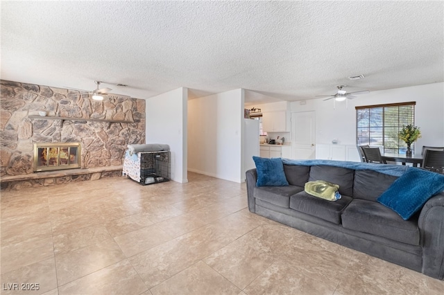 living area with ceiling fan, a fireplace, visible vents, and a textured ceiling