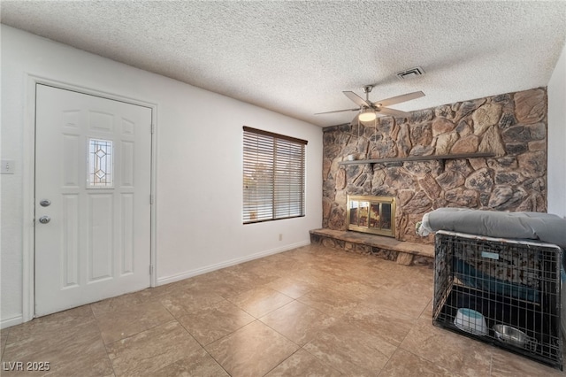 foyer featuring ceiling fan, a textured ceiling, a fireplace, visible vents, and baseboards