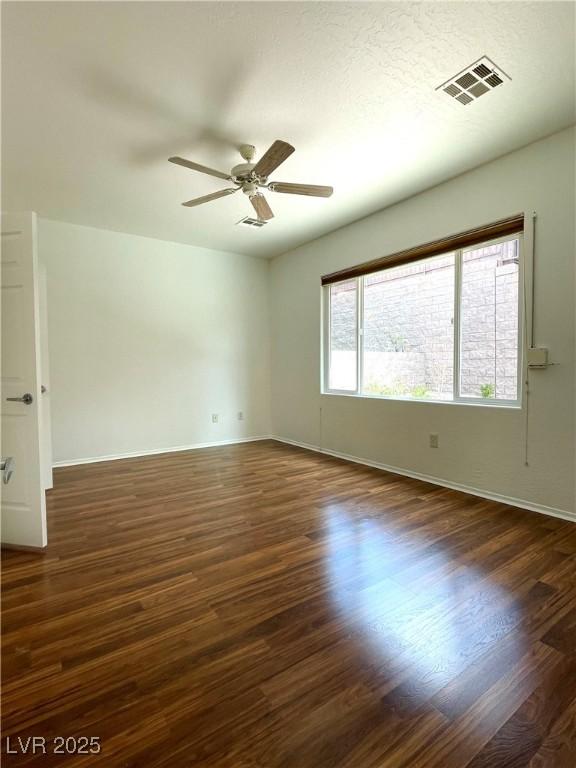 empty room featuring dark wood finished floors, visible vents, baseboards, and a ceiling fan