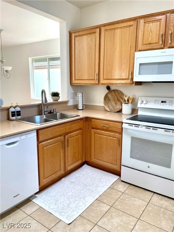 kitchen with a sink, white appliances, light tile patterned flooring, and light countertops