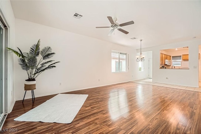 living room with visible vents, ceiling fan with notable chandelier, baseboards, and light wood-style floors