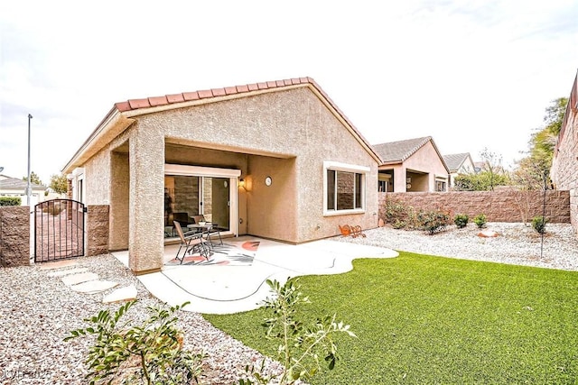 rear view of house featuring fence, stucco siding, a lawn, a patio area, and a gate