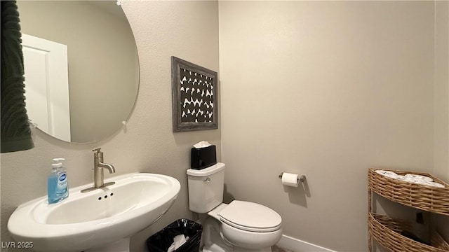 half bath featuring toilet, baseboards, and a sink