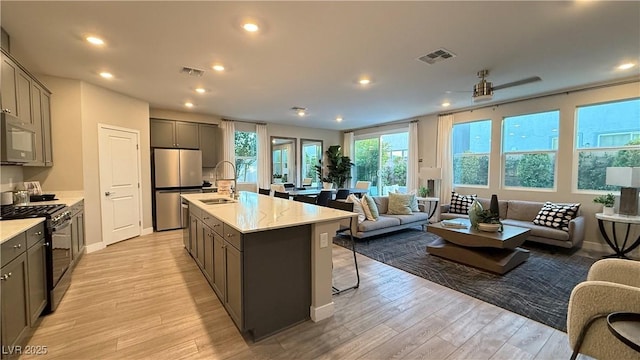 kitchen featuring visible vents, light wood-style flooring, open floor plan, stainless steel appliances, and a sink