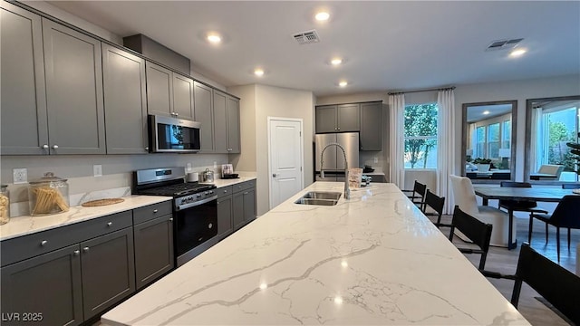 kitchen with light stone counters, stainless steel appliances, a sink, visible vents, and gray cabinets