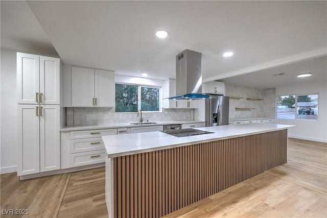 kitchen featuring stainless steel fridge with ice dispenser, island exhaust hood, a sink, light countertops, and backsplash