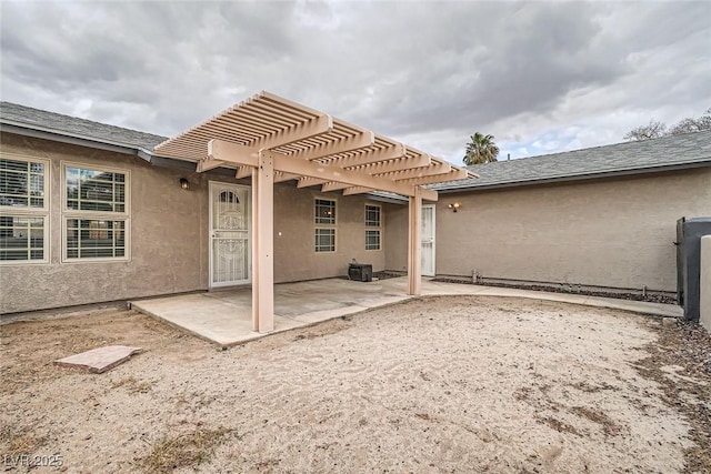 back of property with a shingled roof, stucco siding, a patio area, and a pergola