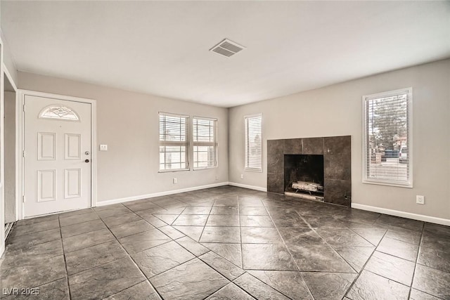 unfurnished living room featuring a tile fireplace, visible vents, and baseboards