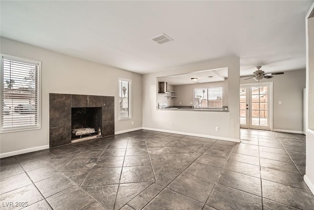 unfurnished living room with ceiling fan, a tiled fireplace, visible vents, and baseboards