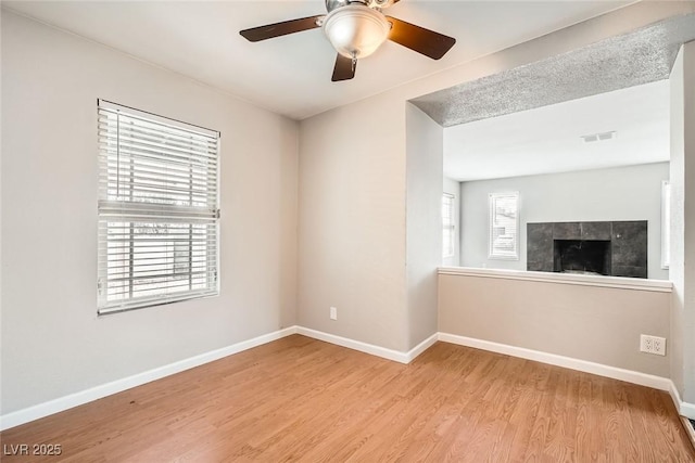 unfurnished room featuring light wood-style floors, a healthy amount of sunlight, visible vents, and a fireplace