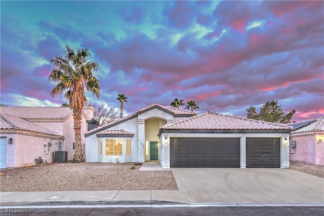 mediterranean / spanish house featuring stucco siding, driveway, a tile roof, cooling unit, and a garage