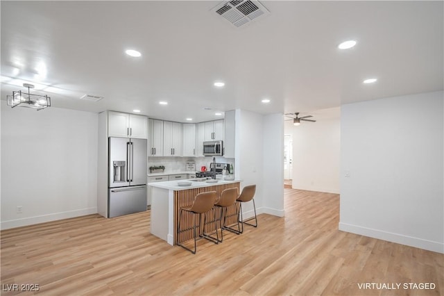 kitchen featuring visible vents, a kitchen bar, a peninsula, light wood-style floors, and stainless steel appliances