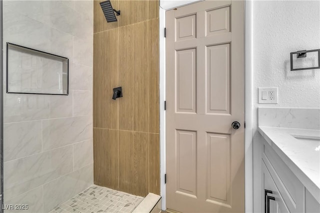 bathroom with a tile shower, vanity, and a textured wall