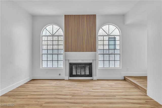 unfurnished living room with a glass covered fireplace, a wealth of natural light, and wood finished floors