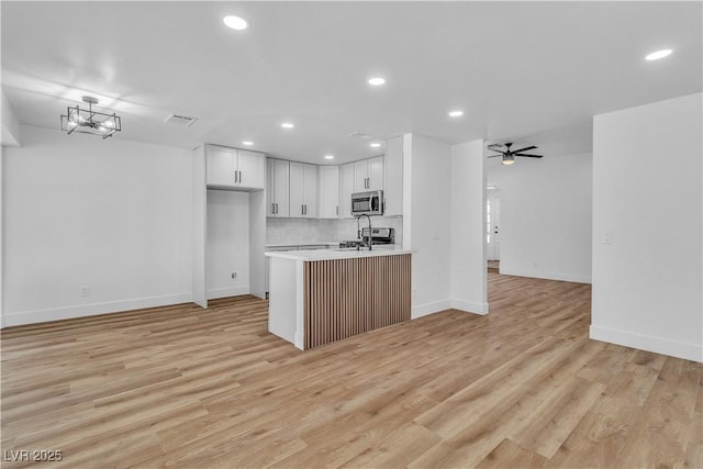 kitchen featuring light wood finished floors, stainless steel microwave, visible vents, open floor plan, and light countertops