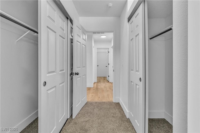 hall with baseboards, visible vents, and carpet floors