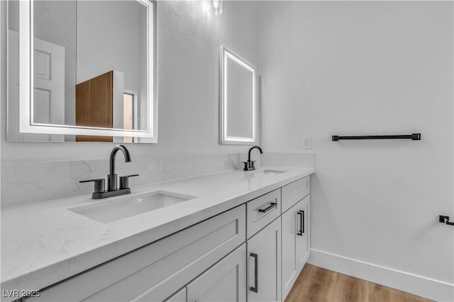 full bathroom featuring a sink, baseboards, wood finished floors, and double vanity