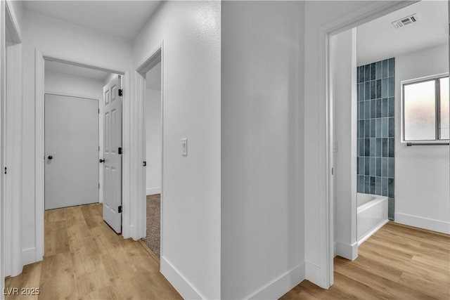 corridor featuring light wood-style flooring, baseboards, and visible vents