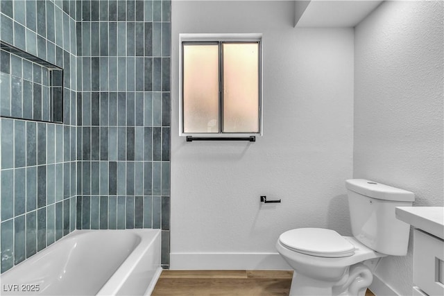 bathroom featuring vanity, wood finished floors, baseboards, toilet, and a textured wall