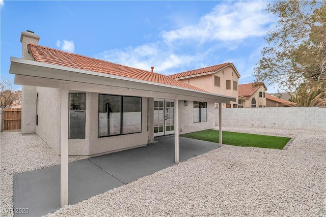 back of property with a tiled roof, stucco siding, a chimney, a fenced backyard, and a patio area