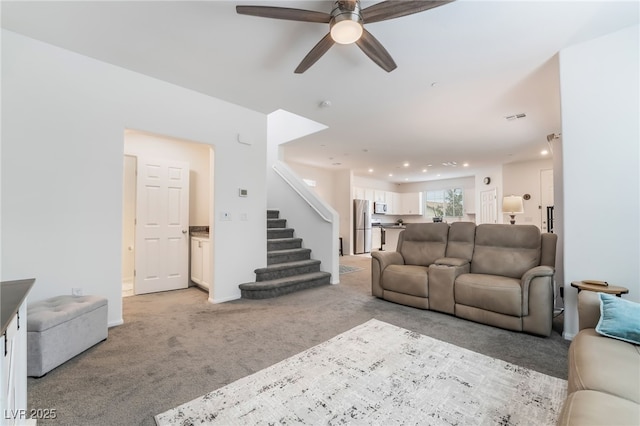 living area featuring ceiling fan, stairs, visible vents, and light colored carpet