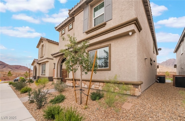 view of side of home featuring central AC, a mountain view, and stucco siding