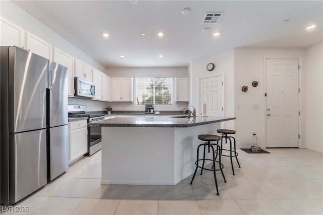 kitchen with a breakfast bar area, stainless steel appliances, recessed lighting, white cabinets, and a kitchen island with sink